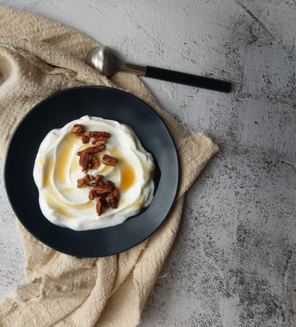 A bowl of yogurt topped with honey and pecans is set upon a dish towel