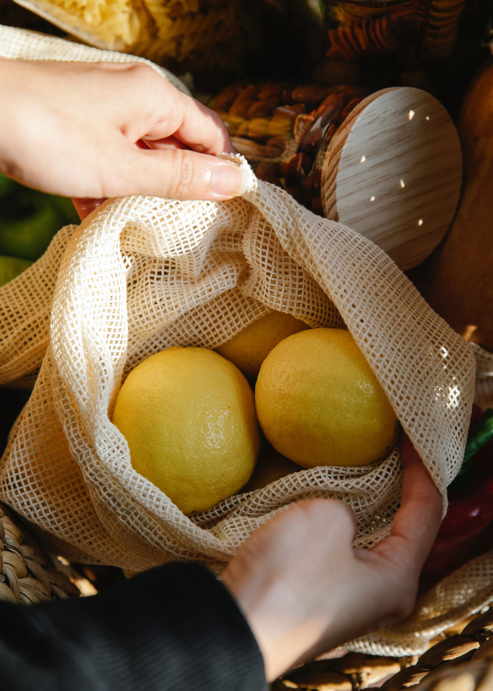 A woman's hands open a cotton reusable bag to reveal fresh lemons. In the background are more farmers market finds.