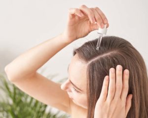 Woman applying castor oil to hair with dropper. 